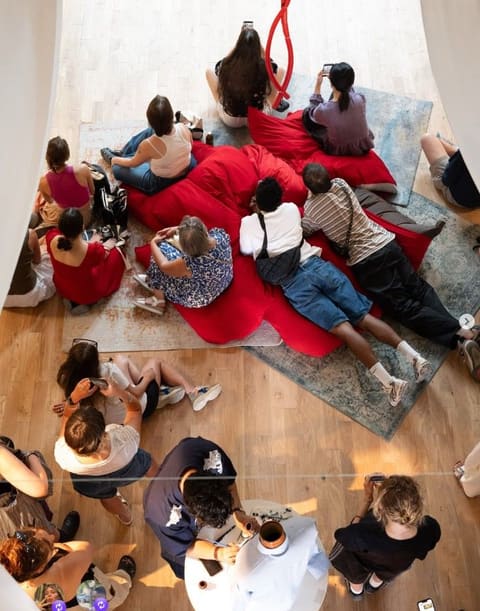 Vue plongeante sur le public allongé et assis sur des coussins rouges pendant une performance à la Chapelle Saint-Lazare.